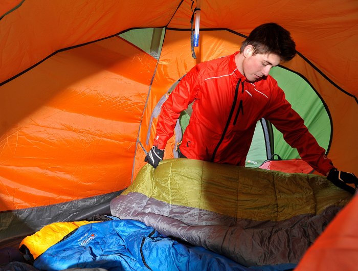 Boy inside orange tent laying out a sleeping bag
