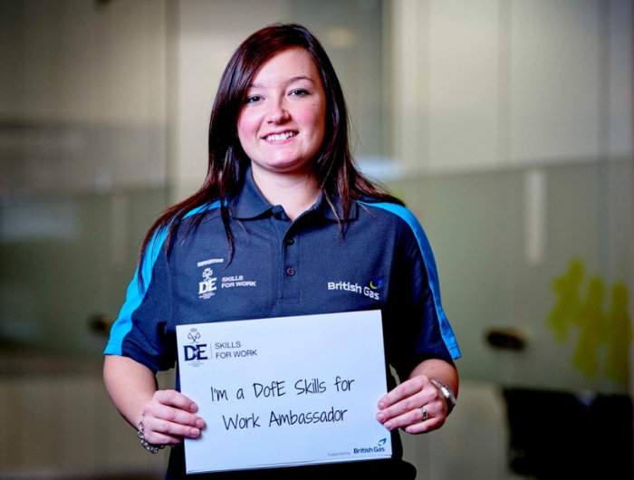 Young woman Alexandra in a British Gas uniform holding a sign saying "I'm a DofE Skills for Work Ambassador"