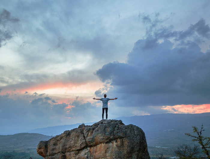 Young man stood on top of rock with arms stretched in the air