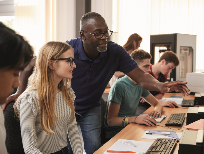 Teacher in classroom showing young girl how to do something on a computer