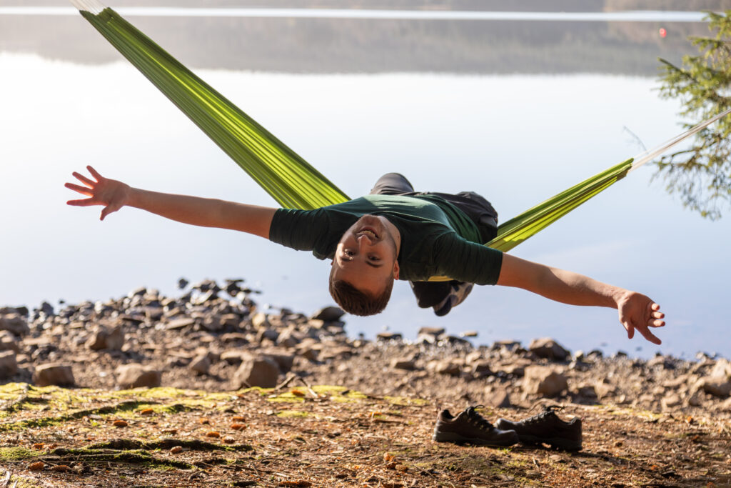 A young person sitting in a hammock leaning back and spreading their arms wide.