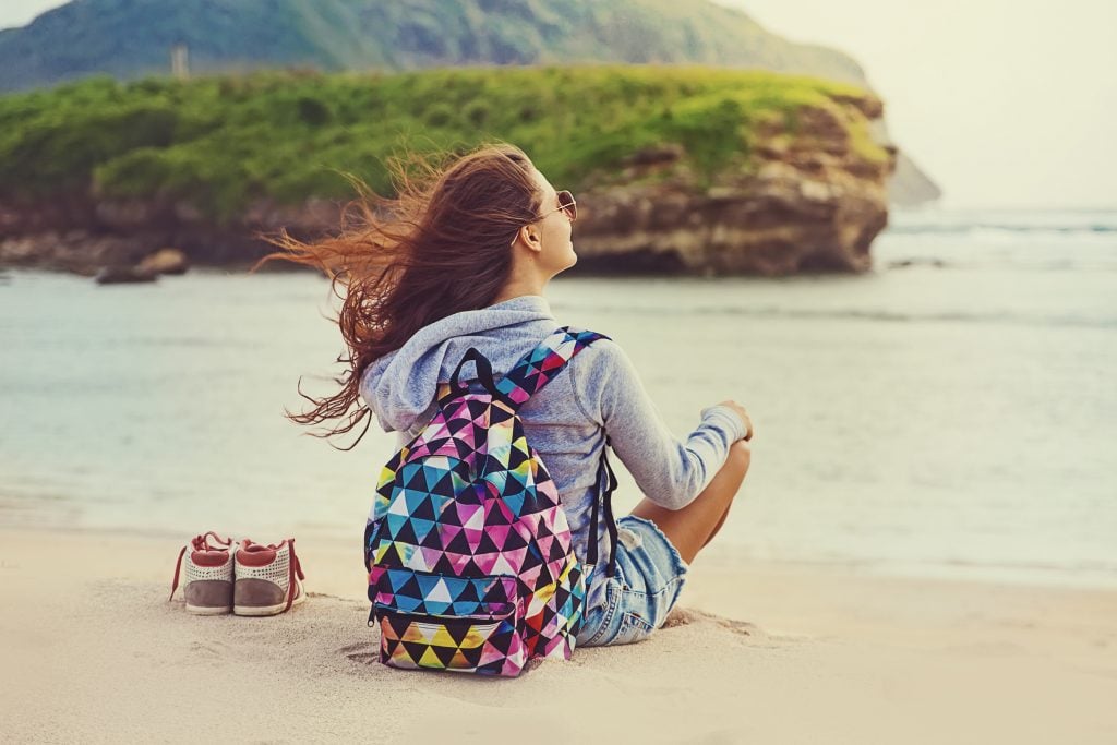 Young woman sitting on beach with backpack