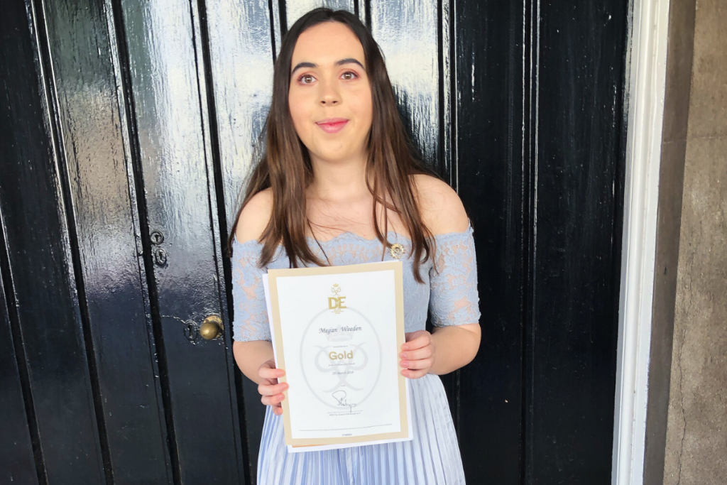 Gold Award holder Megan with her certificate wearing purple dress