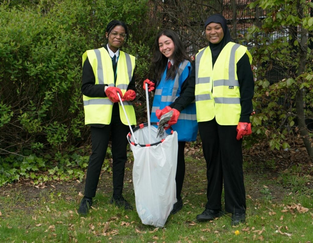 Three young people in school uniforms and high-vis vests doing litterpicking.