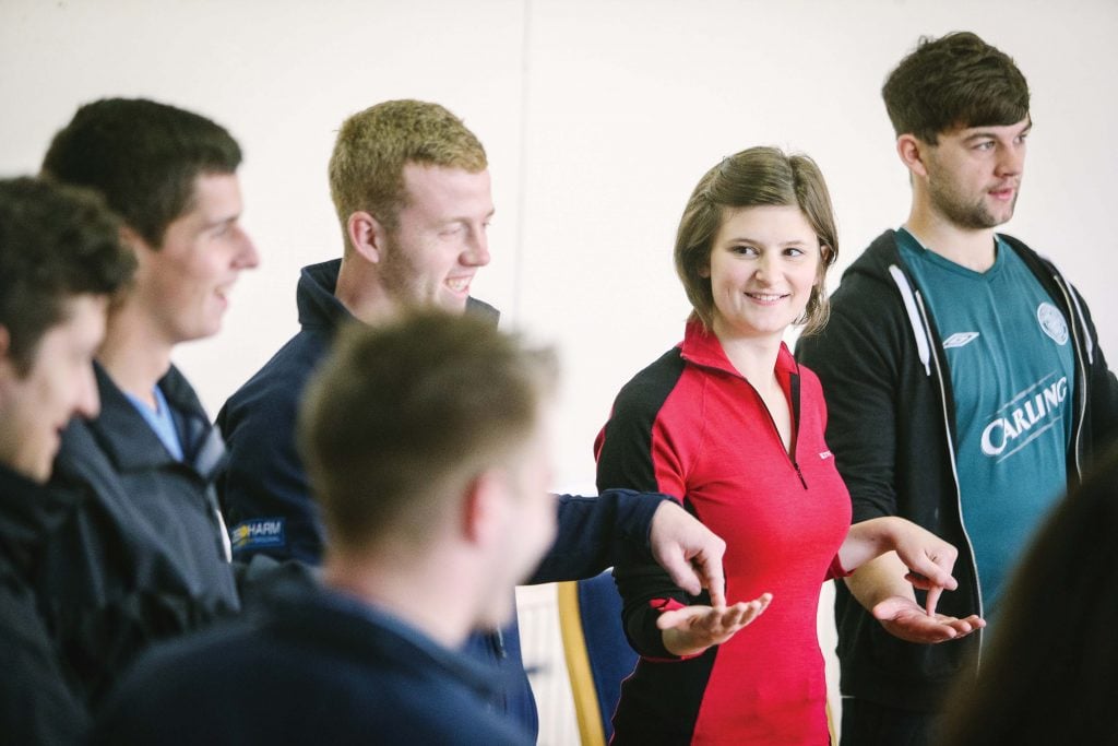 Four young men and one young women taking part in team building exercise and smiling