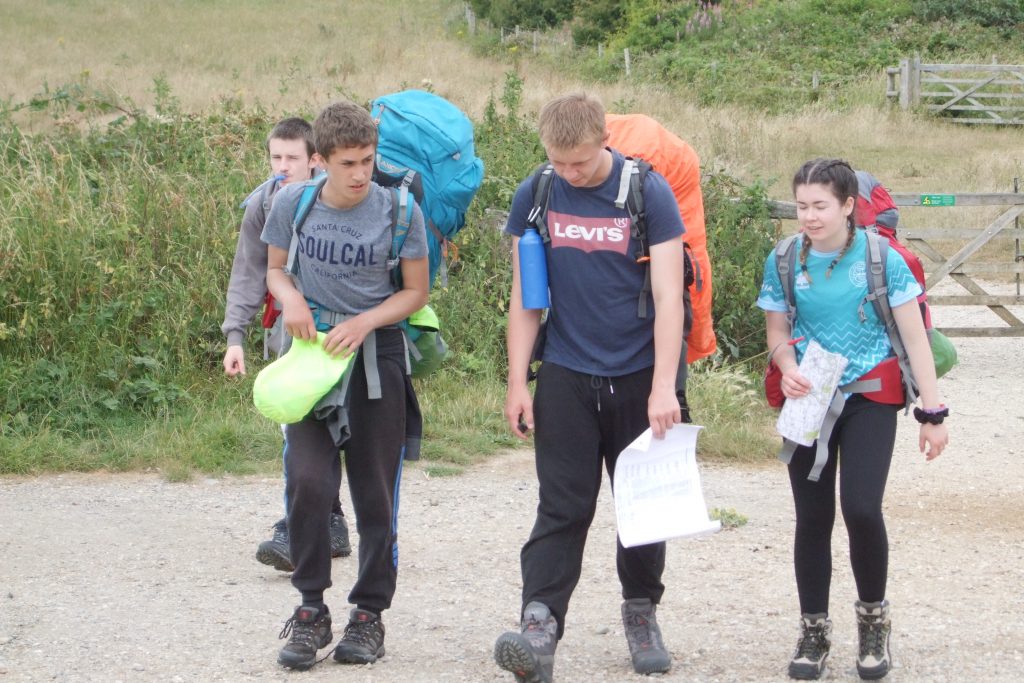 Three young men and one young woman on DofE expedition wearing rucksacks and walking