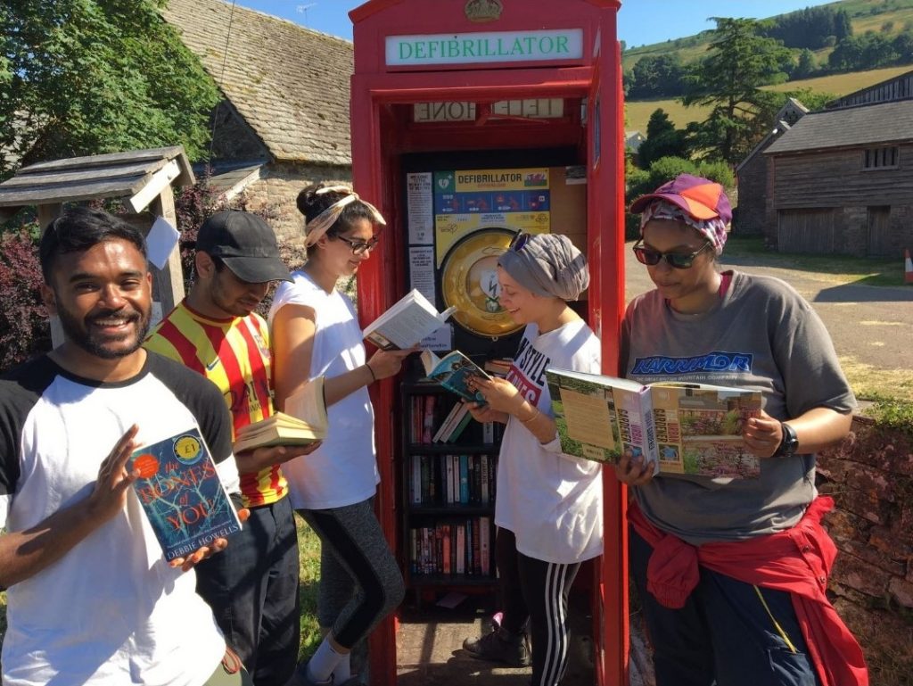 Group of four DofE participants on expedition in front of red telephone box holding maps