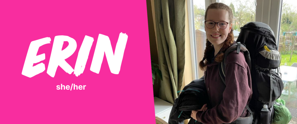 A split design image. On the left, a bright pink background displays the name 'ERIN' in large, white, bold brushstroke-style letters, with 'she/her' written underneath in smaller text. On the right, a person with light skin, glasses, and long, curly brown hair tied into braids is smiling at the camera. They are wearing a burgundy hoodie and carrying a large black backpack with camping gear attached. They are standing indoors near a window, with a garden visible outside.