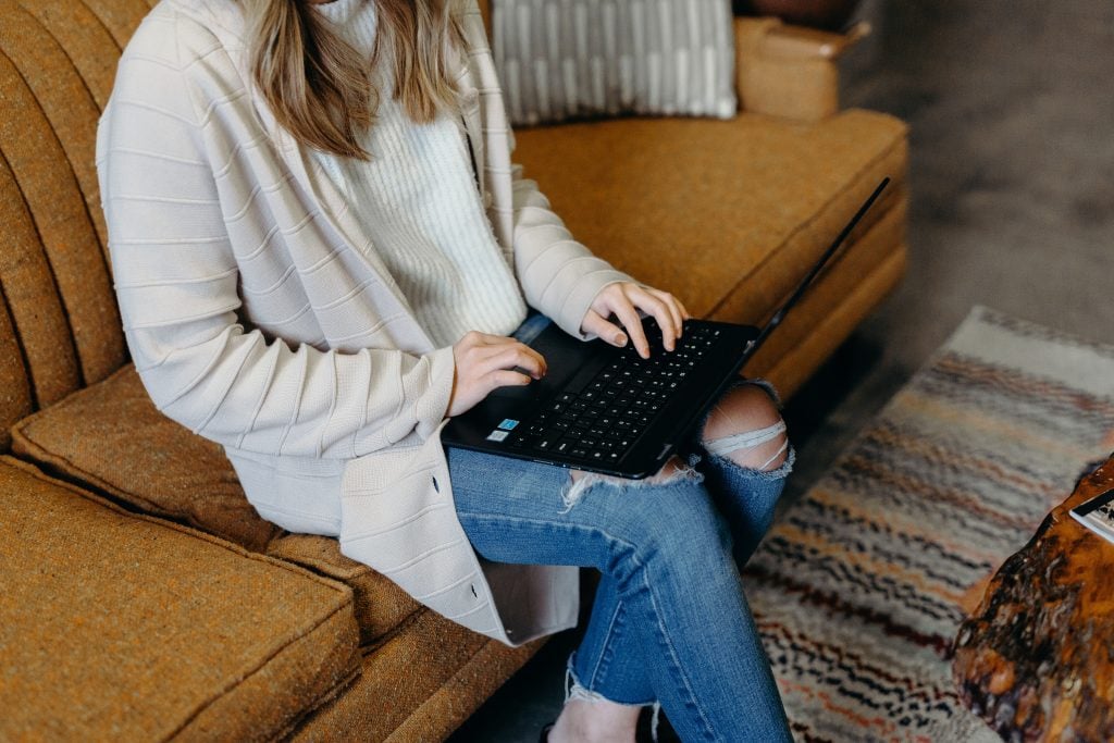 Girl on laptop sitting on beige sofa