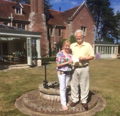 Gordon and Hilary Philips smiling standing in front of their red brick home