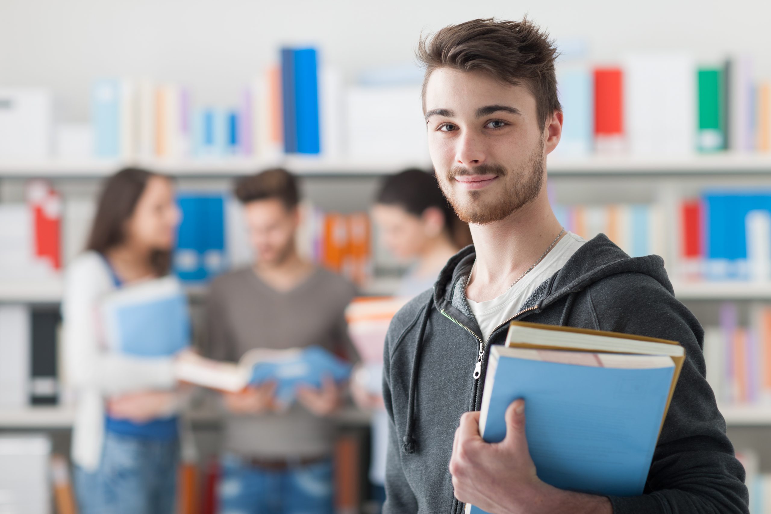 Teenage boy with brown hair holding blue folders in library