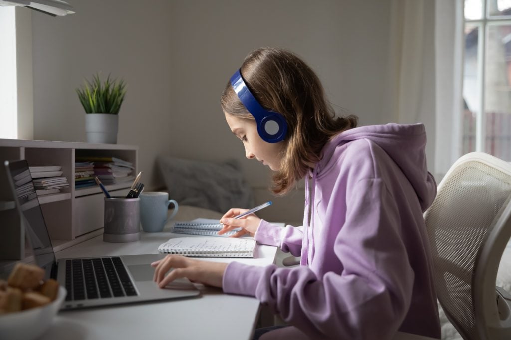 Young person in purple hoodie working at desk with laptop wearing headphones