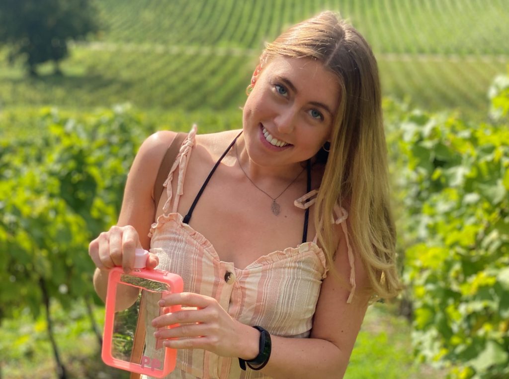 Francesca in sundress in green field holding waterbottle