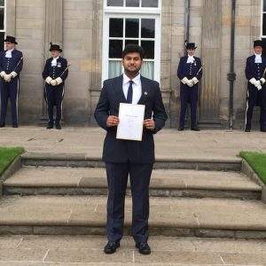 Man standing on steps in front of building holding certificate