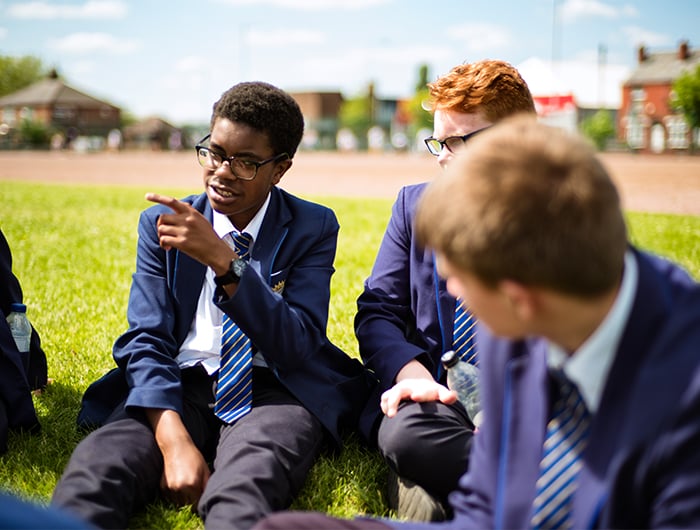 Young people in school uniform sat on grass