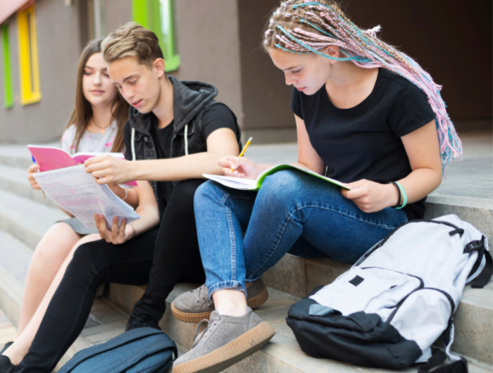 Three young people sitting on a step with workbooks