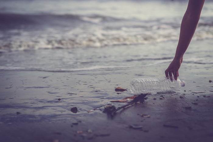 Hand picking up plastic bottle from beach