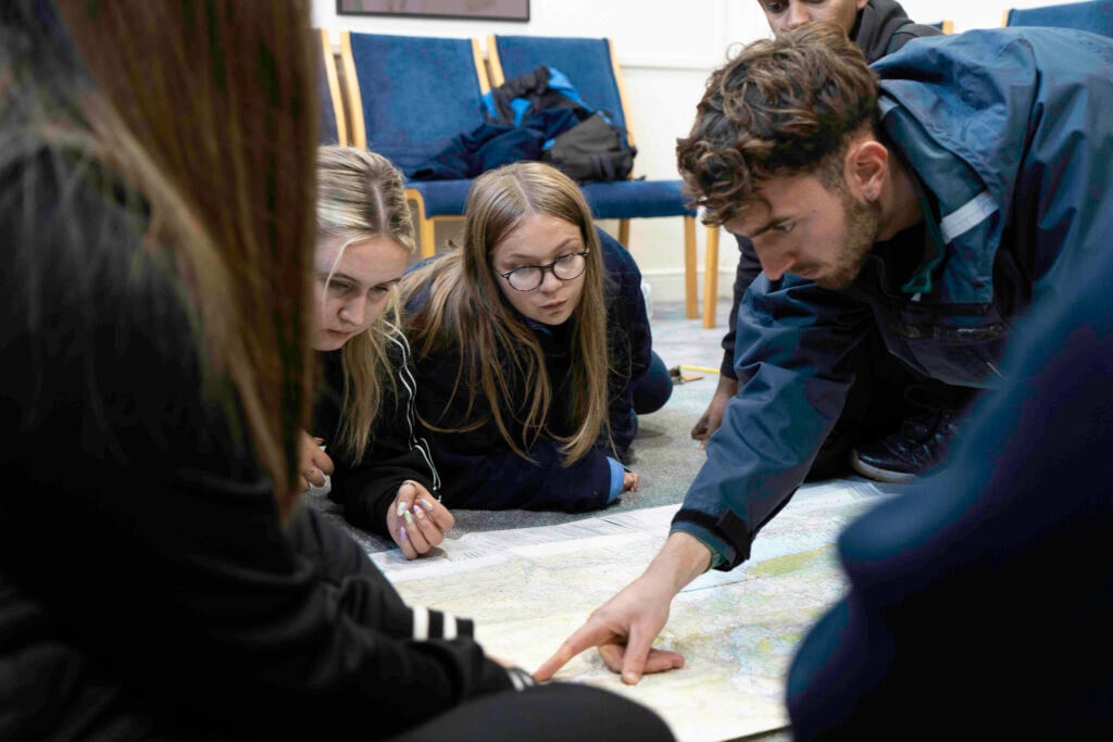Five young people sit on the floor and look at a map planning a route.
