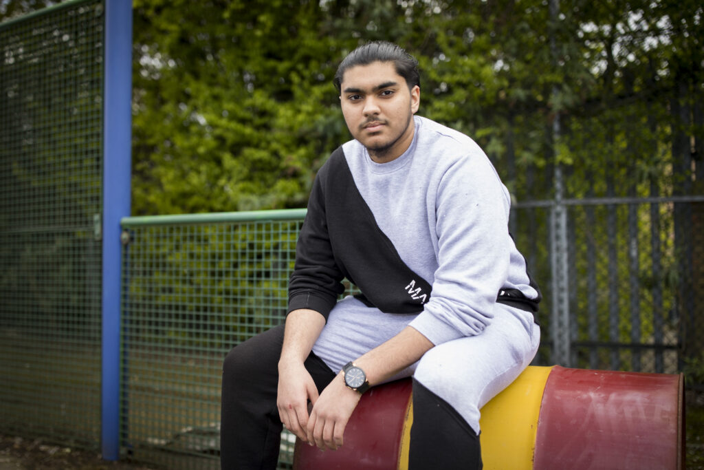 Young person sitting down in an outside court with trees in background. 