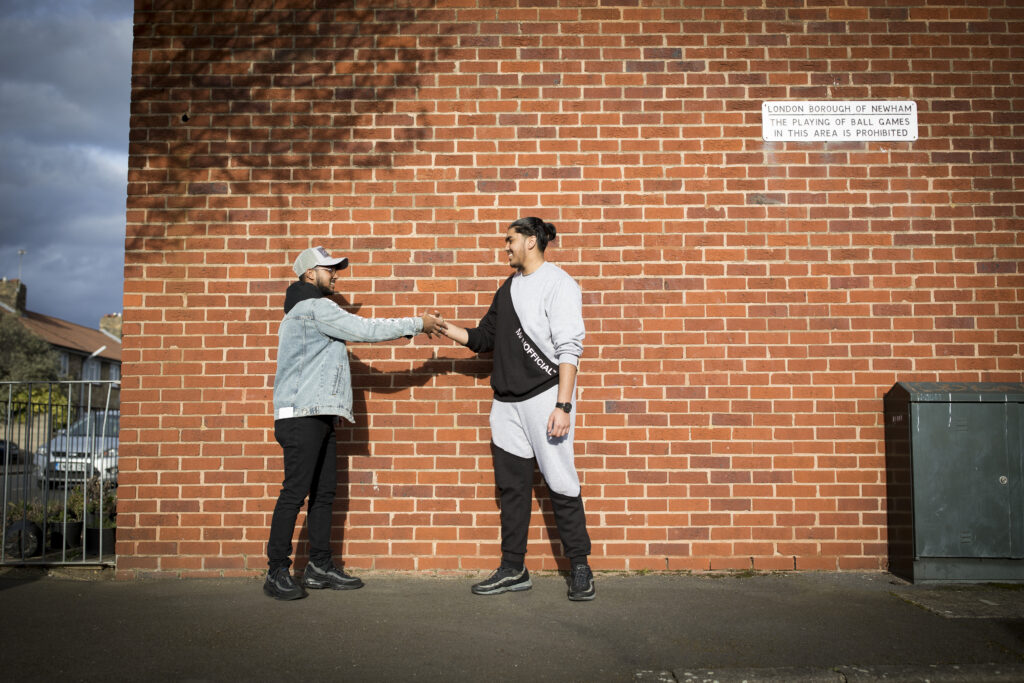 Two young people standing in front of brick wall shaking hands.