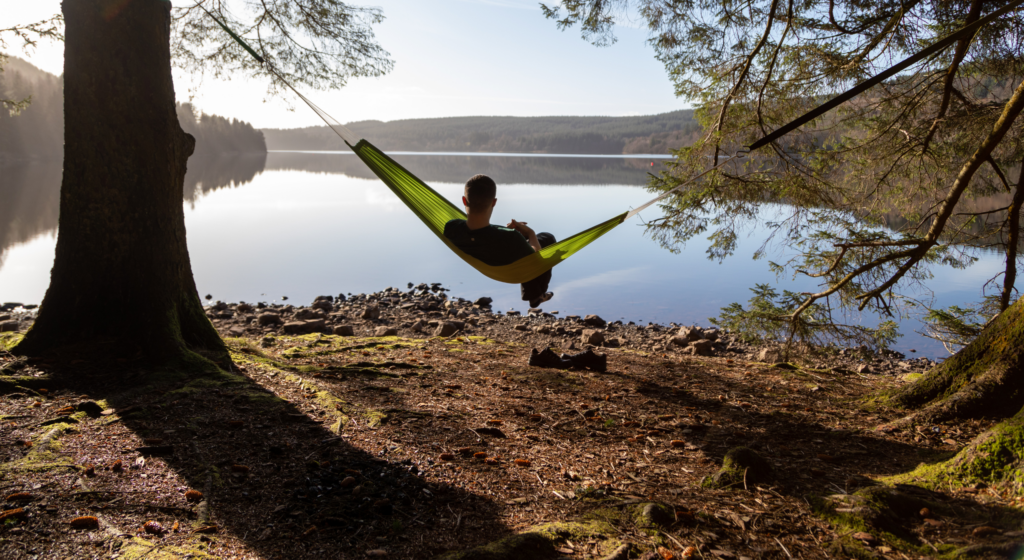 A young person sitting in a hammock looking out over a still lake.