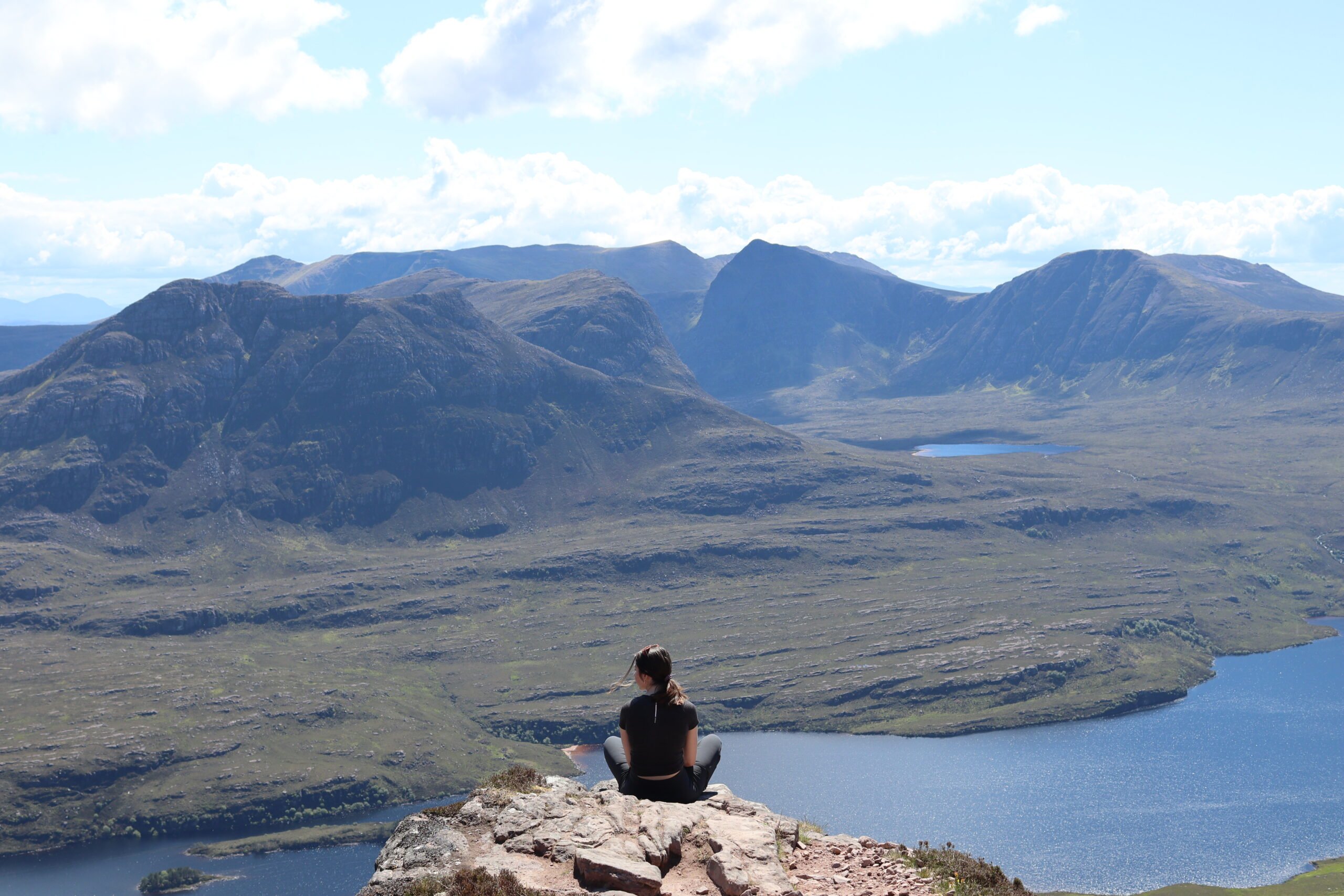 Amiee on cliff overlooking gorgeous mountains in the distance and a body of water