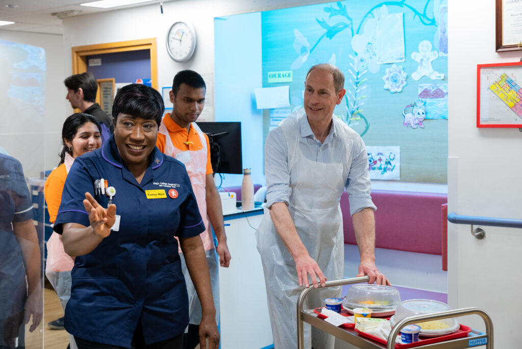 HRH The Duke of Edinburgh wheeling a trolley next to staff in King's College Hospital.