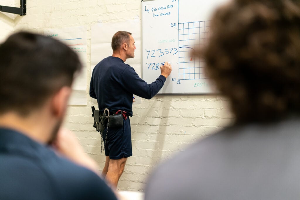 A prison officer writes on a whiteboard in front of young offenders.