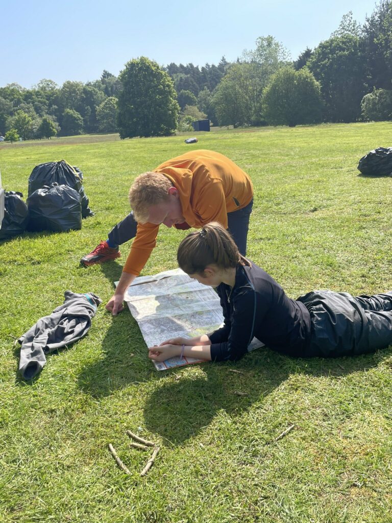 Bea lying on the grass reading a map with an instructor.