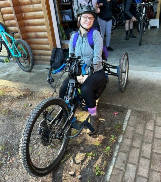 Emma sitting on a three-wheel bike wearing a helmet and smiling.