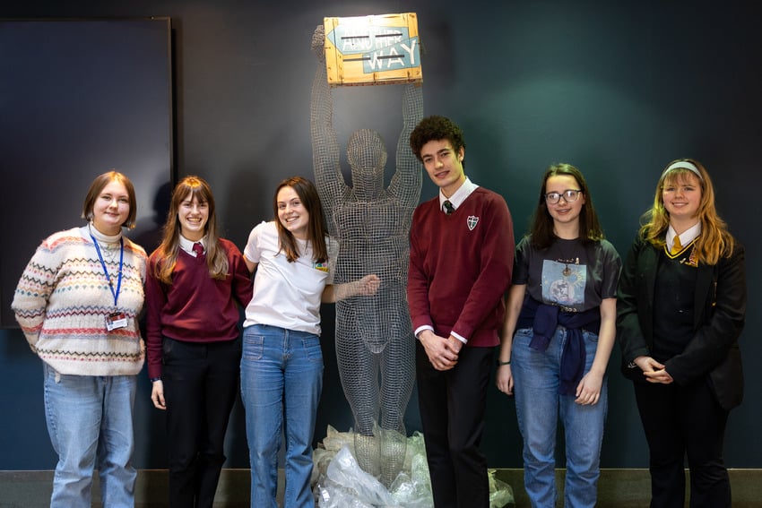Six people standing next to a statue holding a sign that says "Another Way".