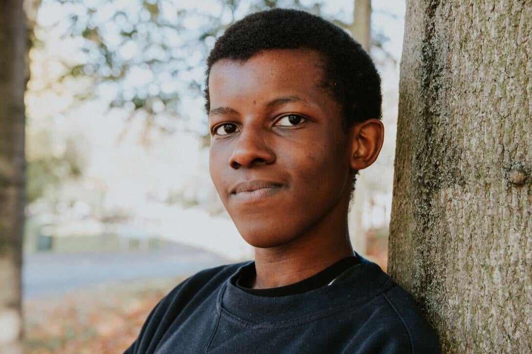 Christopher leaning against a tree trunk looking into the camera