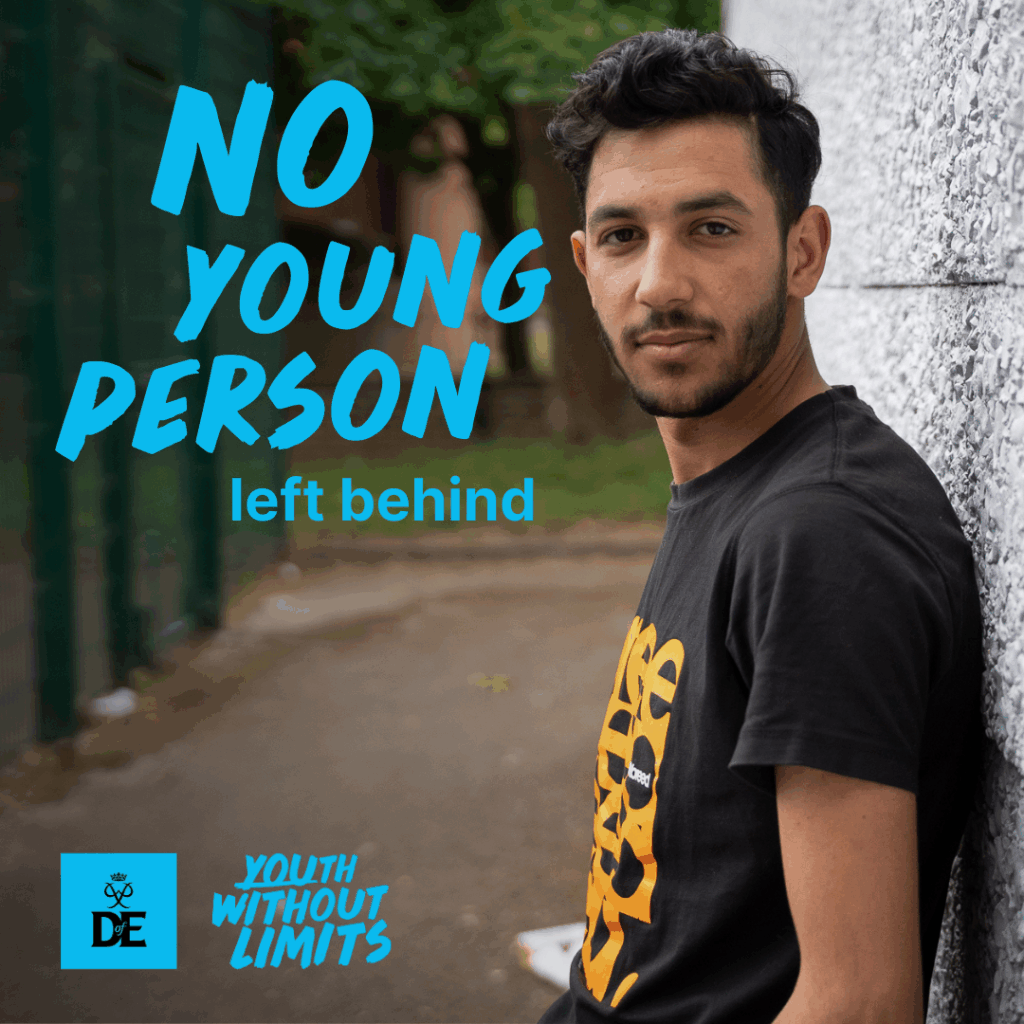 Alyas with short dark hair and a trimmed beard stands leaning against a light-colored wall, looking confidently at the camera. He is wearing a black t-shirt with an orange graphic design. The background shows a pathway lined with a fence and trees. Blue text on the image reads: "NO YOUNG PERSON left behind". Logos at the bottom include "DofE" (The Duke of Edinburgh’s Award) and "Youth Without Limits".