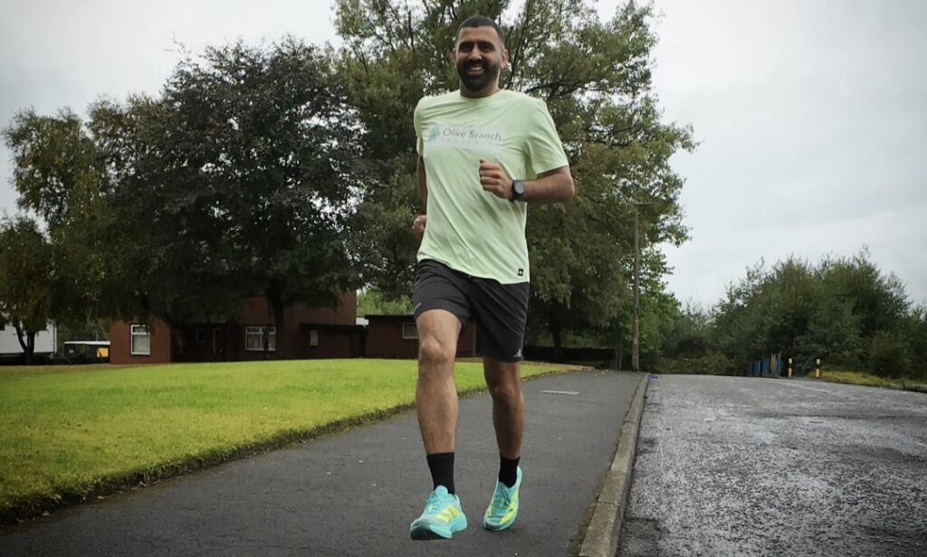 Raja smiles while running down a road wearing a green tshirt with Olive Branch Fostering's logo