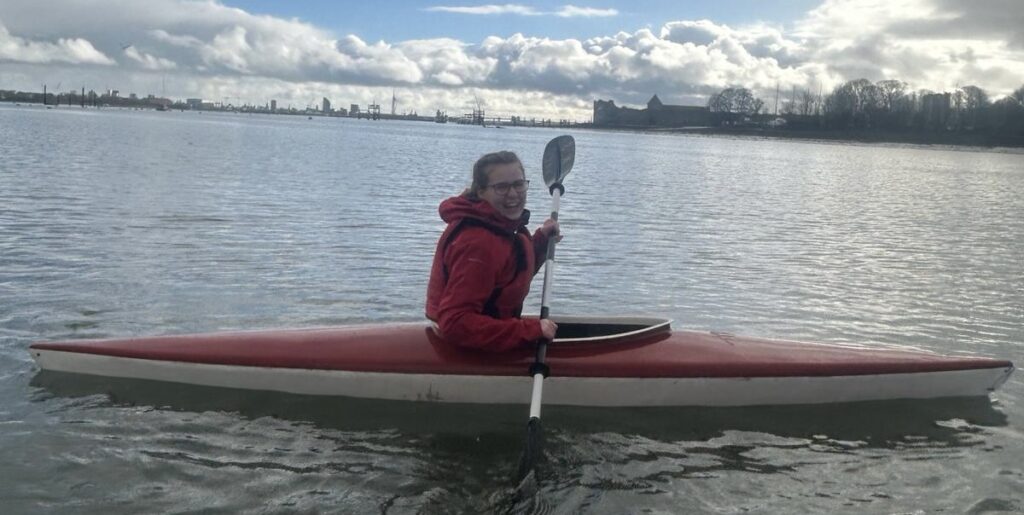 Anais smiles while sitting in a red kayak holding a paddle.