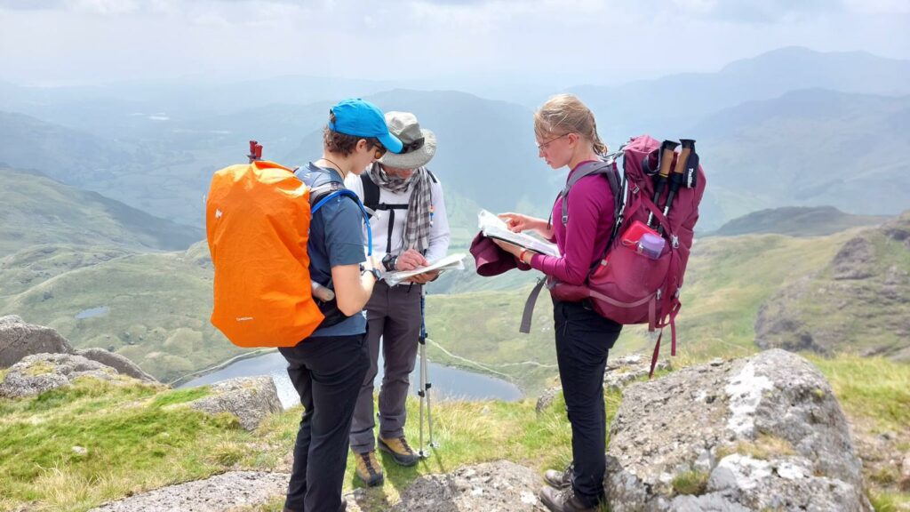 Hannah on a mountain reading a map with two other D of E participants.