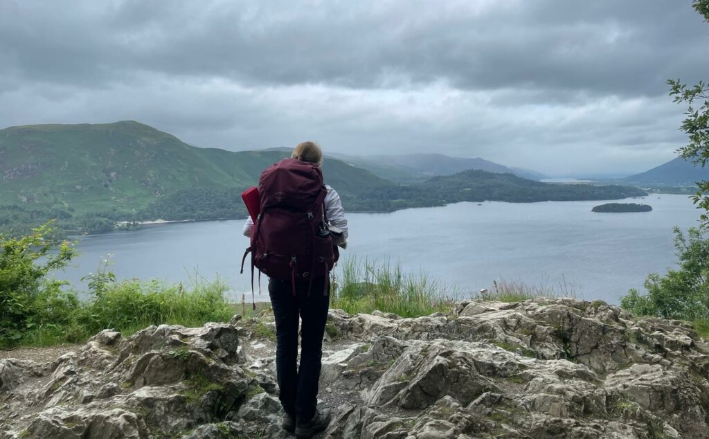 Hannah carrying a rucksack looking out on a view of a lake from a mountain.