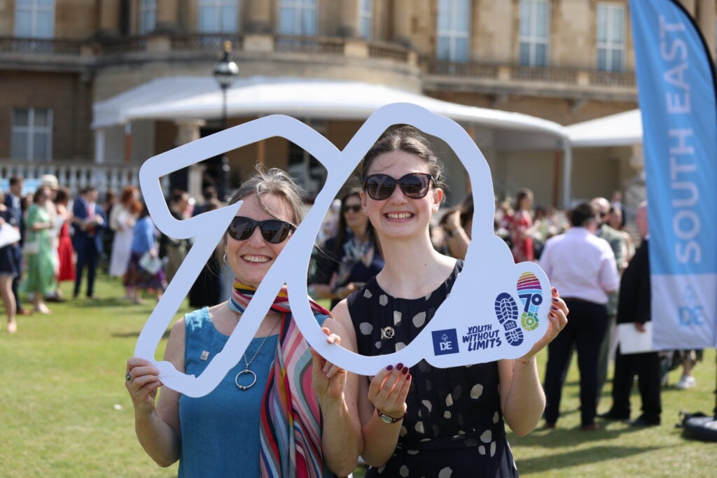 Two young people holding a sign that outlines the number 70 with their smiling faces in the numbers.