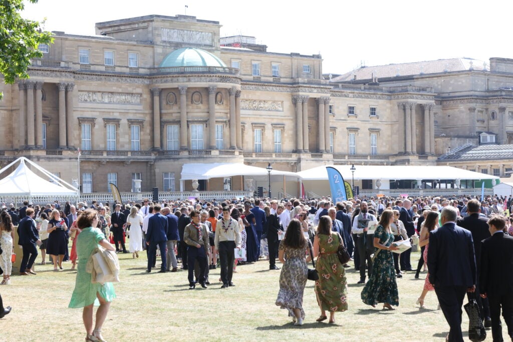 Buckingham Palace Gardens filled with people for the Gold Award Celebrations with Buckingham Palace in the background.
