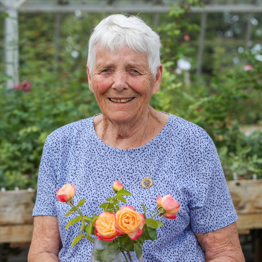 DofE Alumna Gillian holding a pink and yellow rose in a clear glass vase