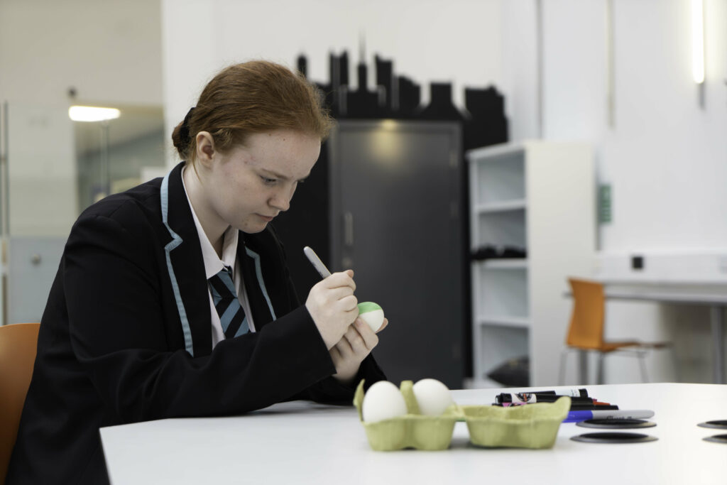 A young person in a school uniform sitting at a table decorating an egg.