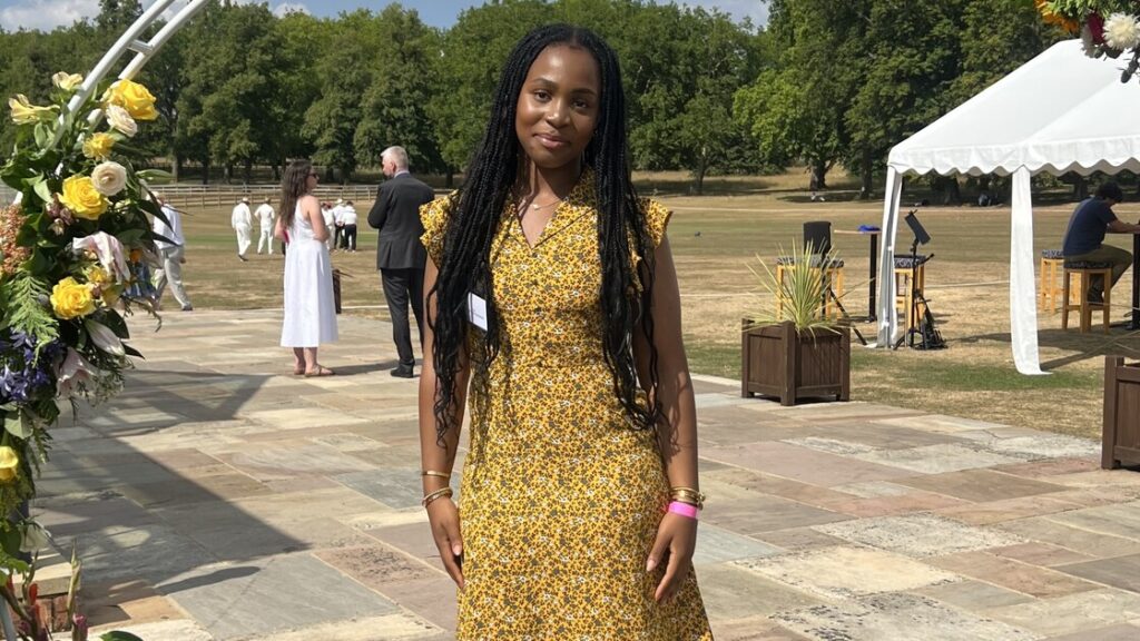 Faith is standing in a garden wearing a yellow dress.