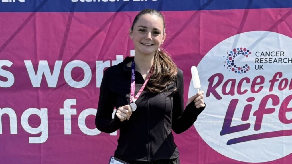 Jenna is smiling holding a medal after finishing Race for Life.