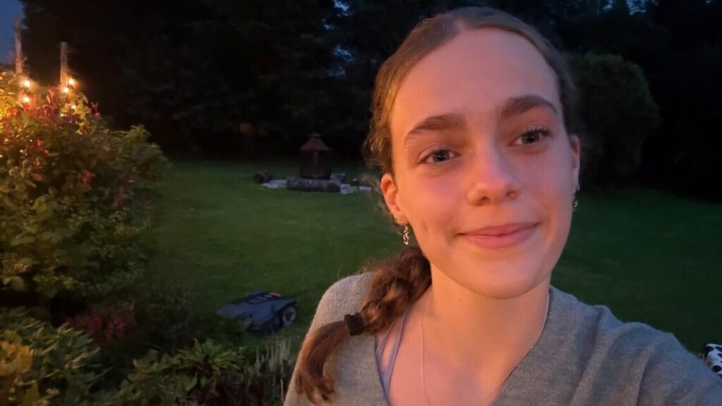 Niamh has brown hair in a plait, she's standing in a garden.