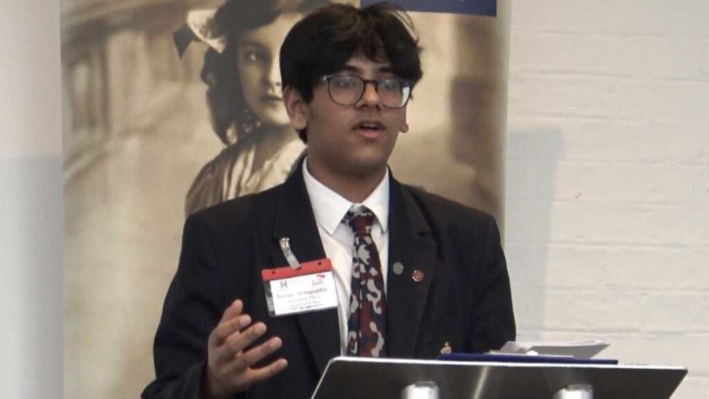 Sathya is wearing a suit, standing at a podium talking.