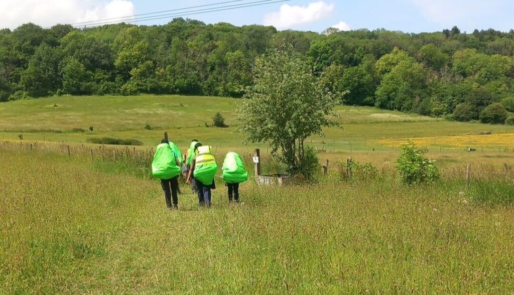 Three DofE participants walking across a grassy field on expedition.