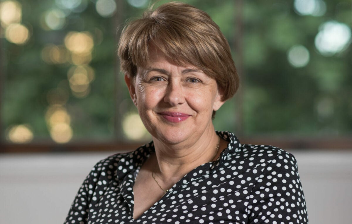 Tanni smiling and sitting in her wheelchair wearing a black dress with white spots.