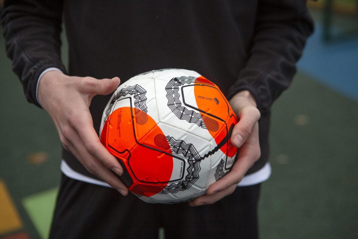 A pair of hands holding a white, orange and black football.