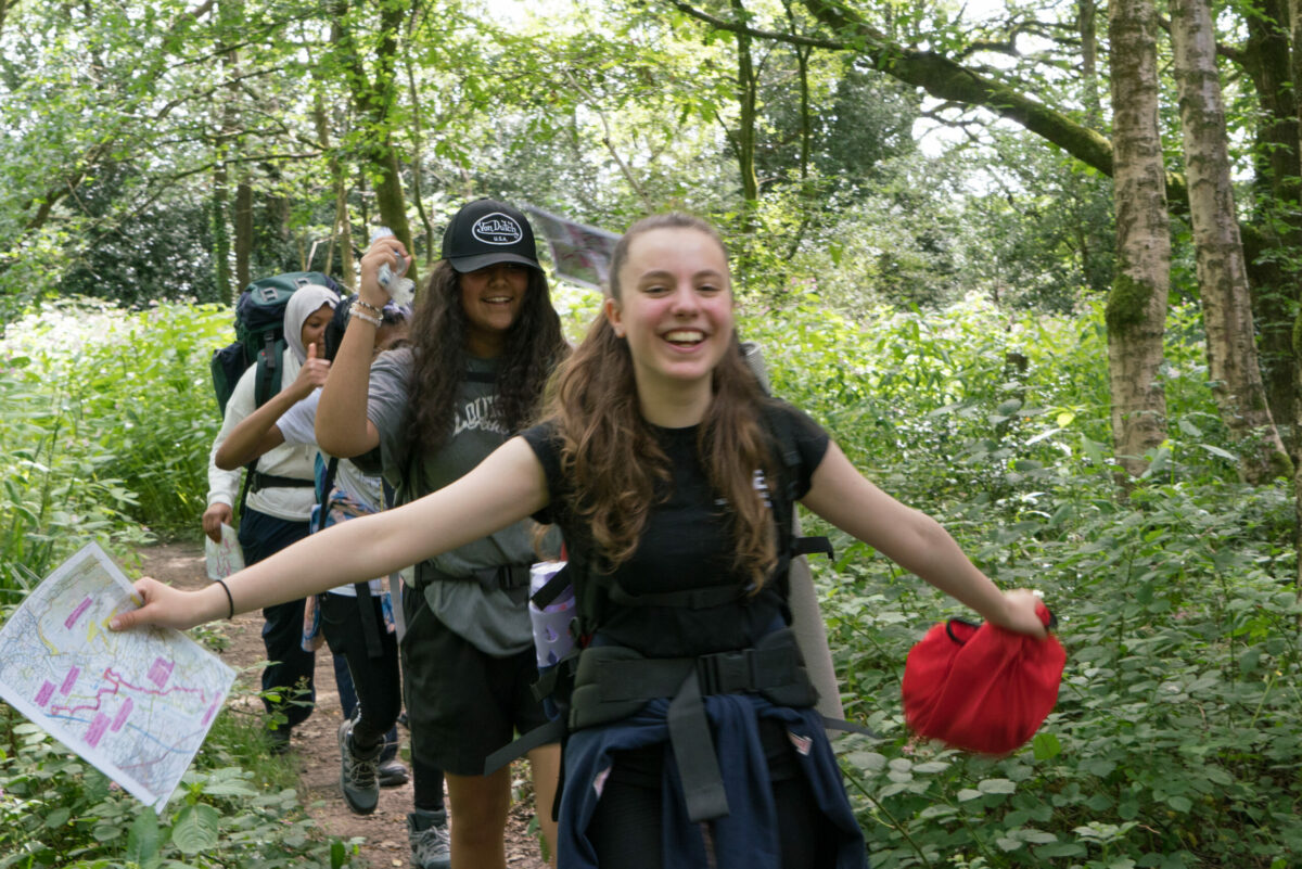 Young people walking along a path holding maps and smiling.