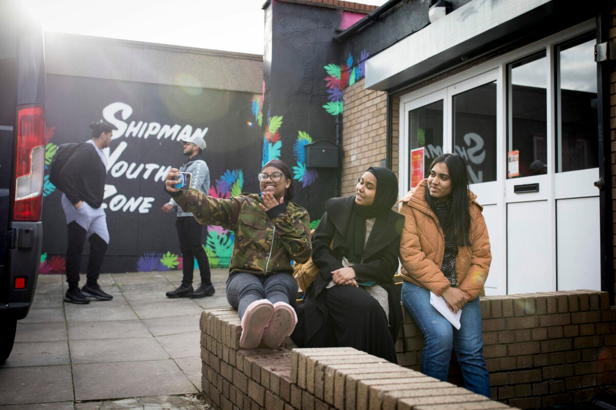 Three young people sitting outside a youth club taking a selfie.